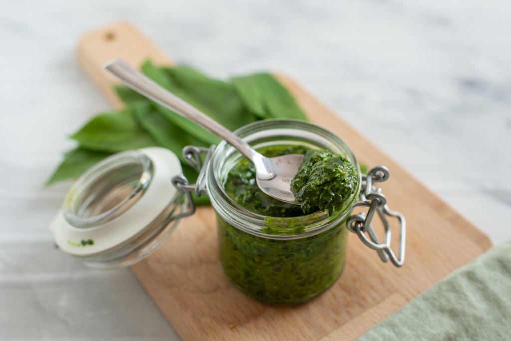 pumpkin seed pesto in jar with spoon on cutting board with basil