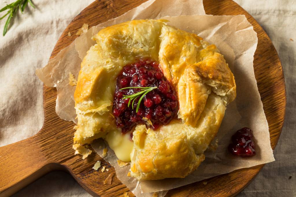 homemade baked brie with jam on cutting board as part of a roundup of thanksgiving appetizers