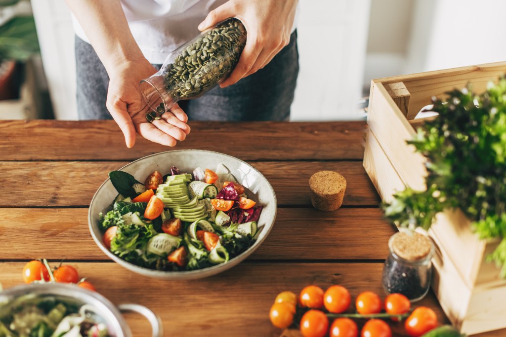 woman adding pumpkin seeds to a healthy salad in kitchen