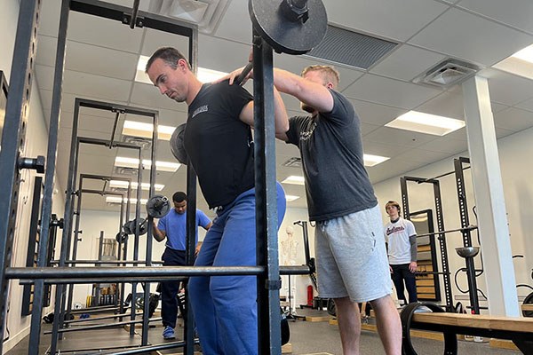 andrew checks the bar position on a lifter in the squat