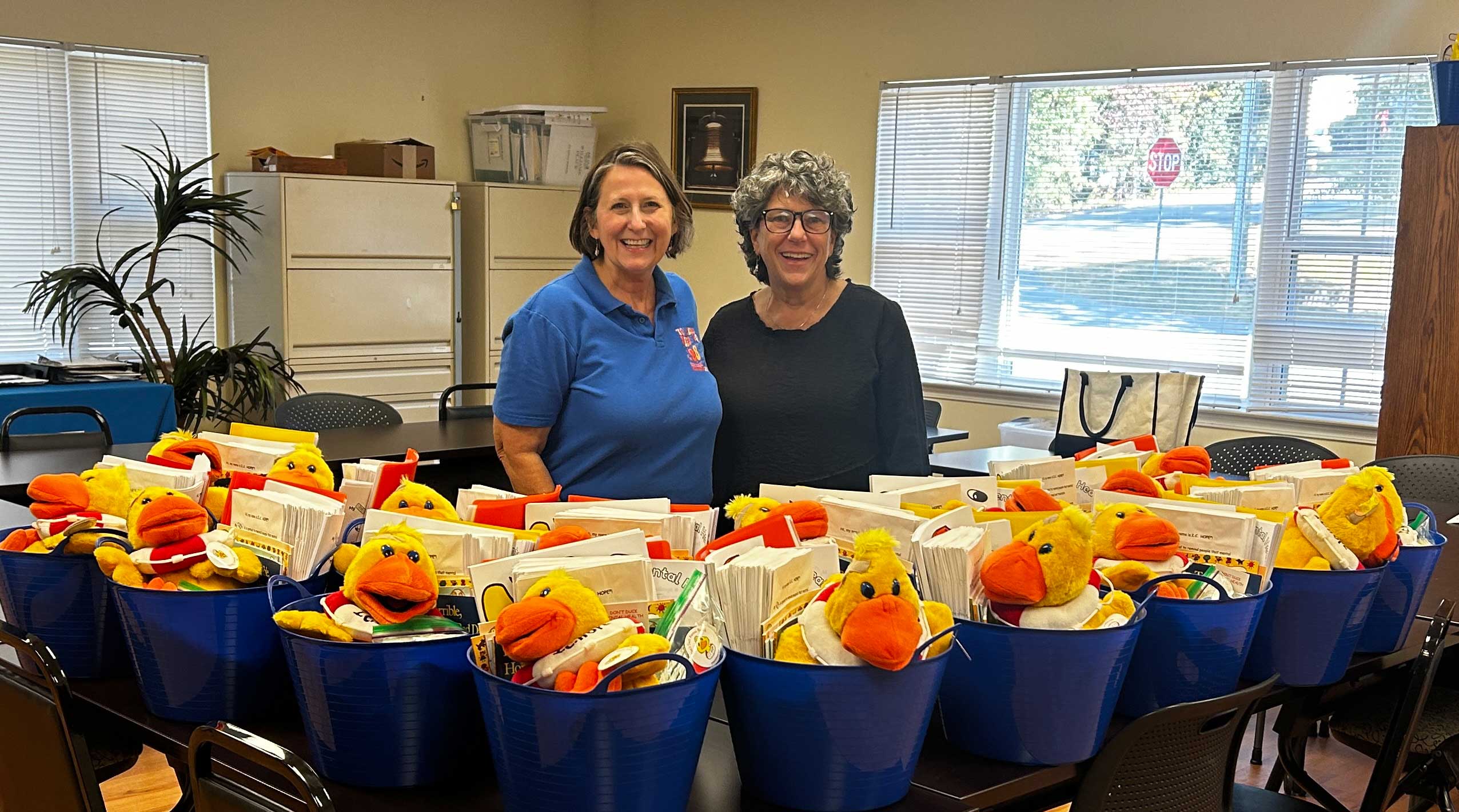 volunteers stand with buckets of mental health resources on tables in front of them