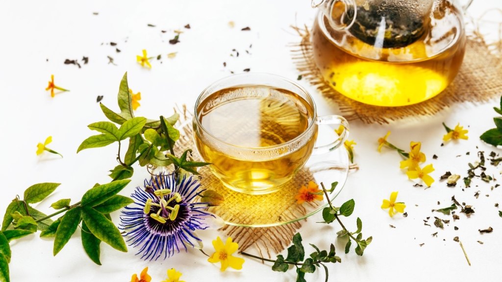 A clear glass cup of passionflower tea beside a purple flower, which helps when you can't sleep at night