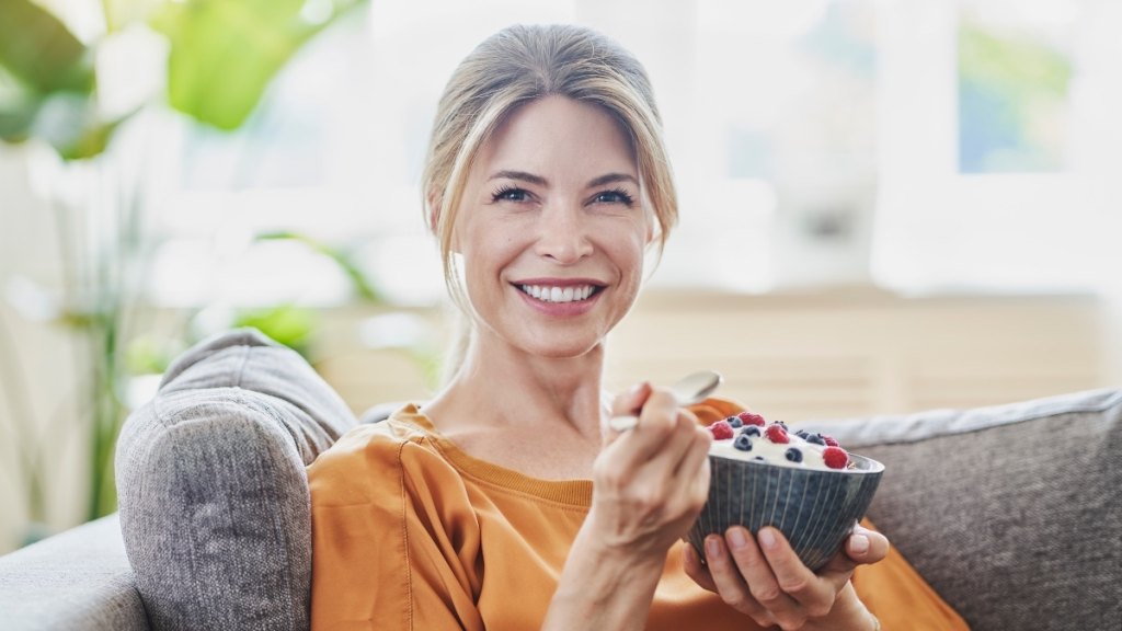 A woman in a gold shirt holding a bowl of yogurt, which can balance vaginal pH naturally