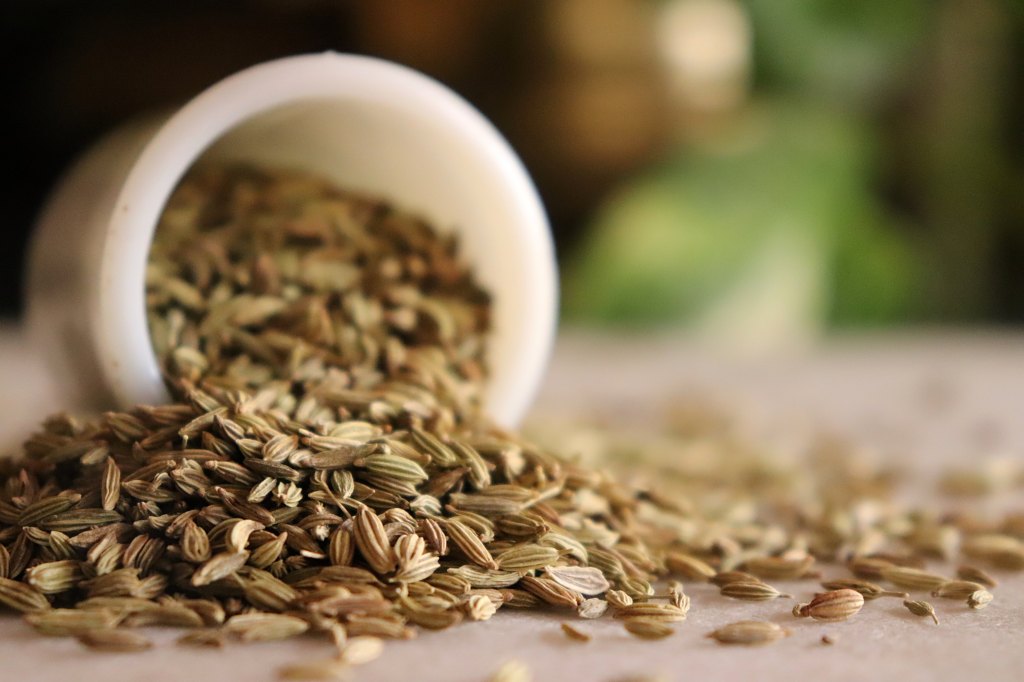 Close-up of fennel seeds(saunf) pouring out from a ceramic bowl