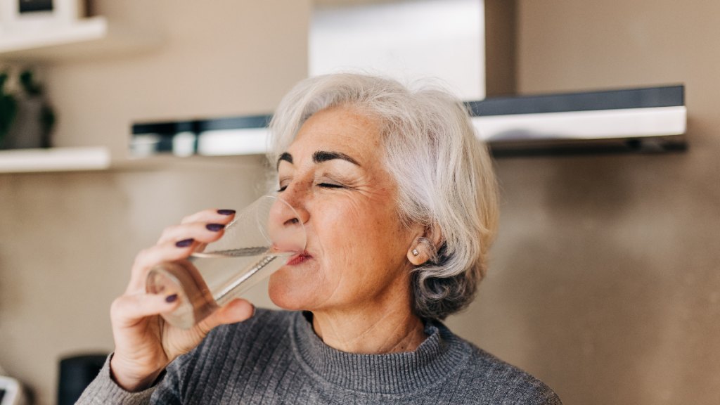 older woman drinks a glass of water as she treats and prevents UTIs