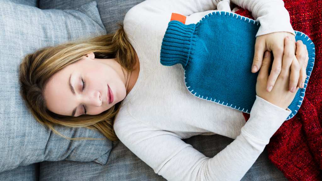 woman lies down, hugging hot water bottle as she soothes her UTI