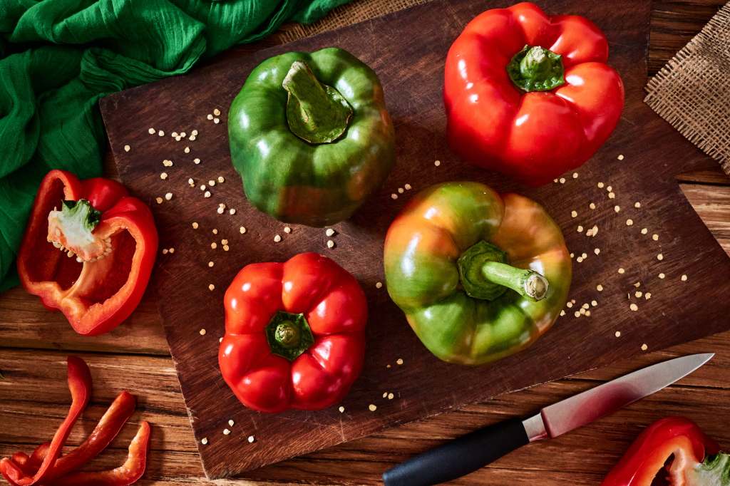 fresh red and green bell peppers on wooden cutting board