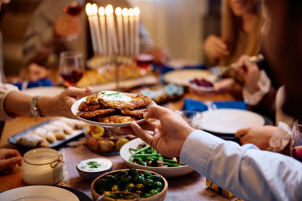 Close up of Jewish people passing latkes during traditional Hanukkah dinner at dining table