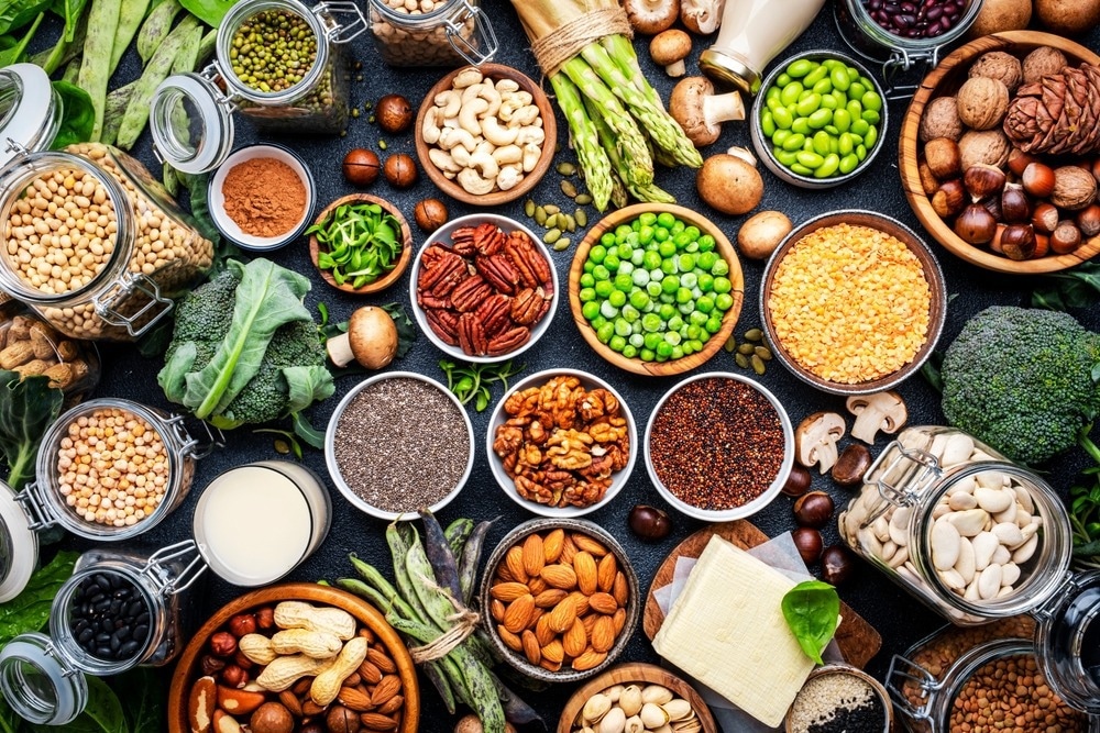 Top view of legumes, beans, lentils, nuts, soy milk, tofu, cereals, seeds and sprouts on black table