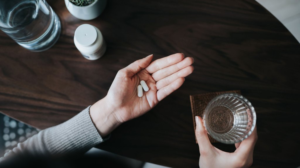 Woman holding pills in hand with water