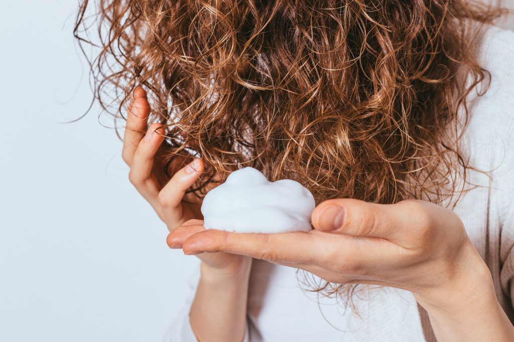 woman putting mousse in thin, curly hair