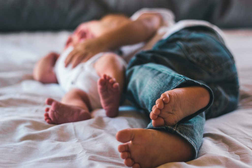 An adult sleeps beside a baby on a bed.