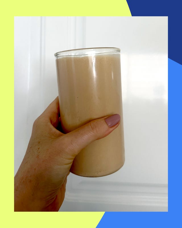 a hand holding a glass filled with a creamy brown beverage against a colorful background