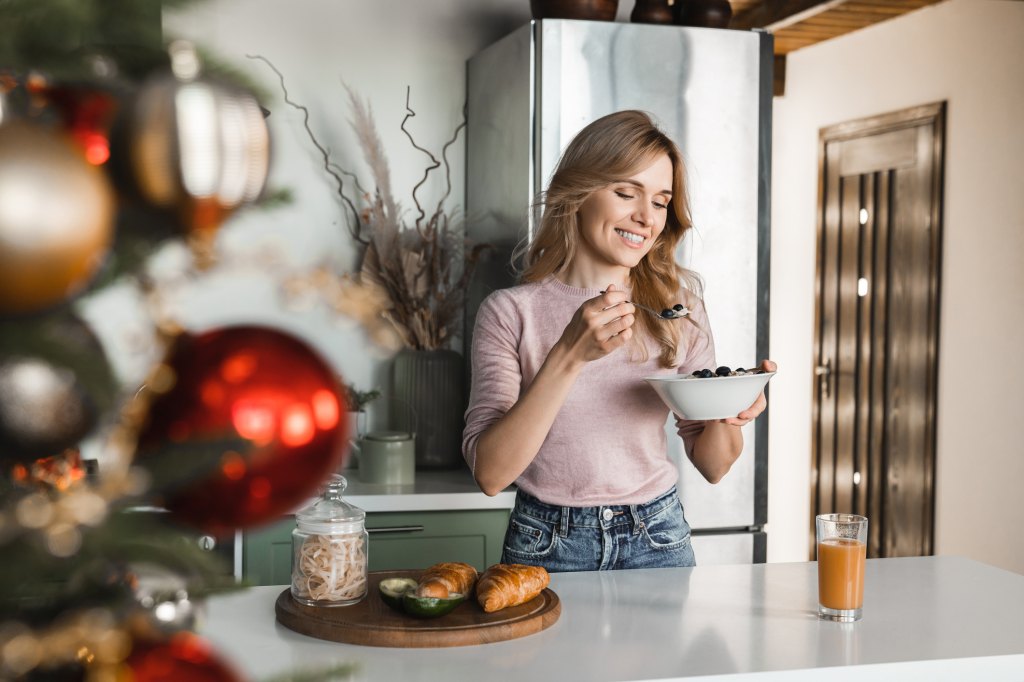 cheerful woman on Ozempic standing in the cozy kitchen eating healthy breakfast during the holidays