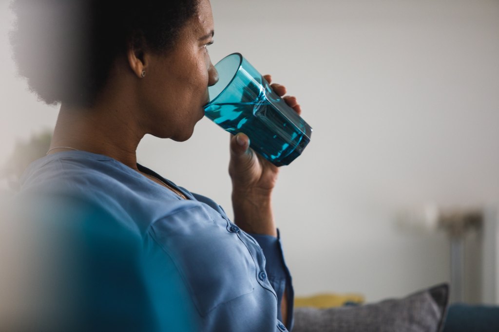 mature woman drinking a glass of water to treat the 24-hour flu