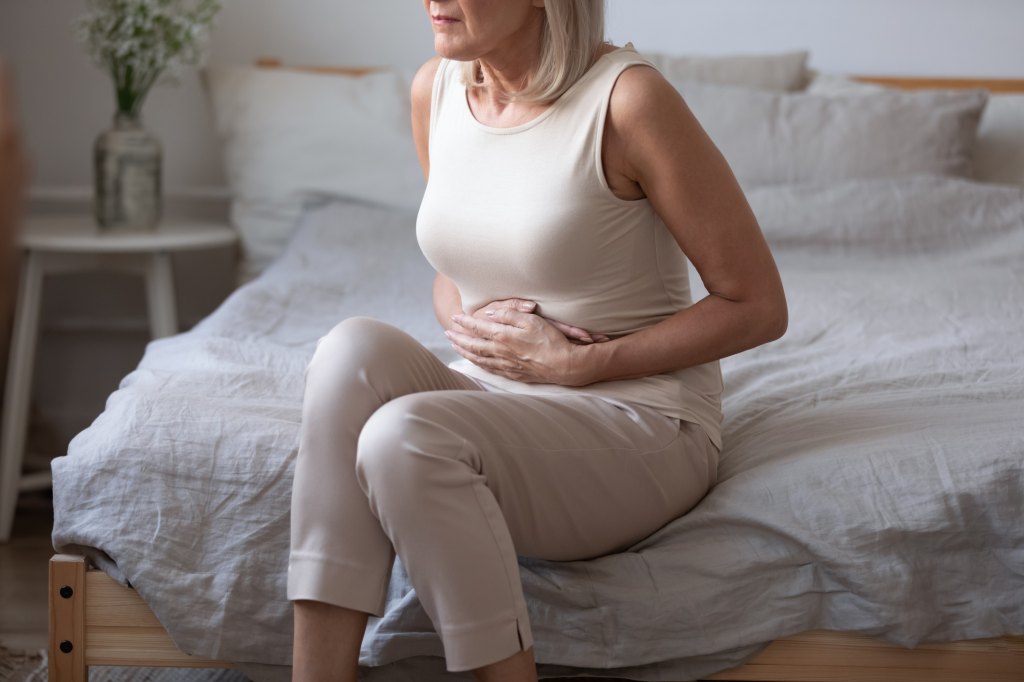 mature woman clutching her stomach on her bed due to the 24-hour flu