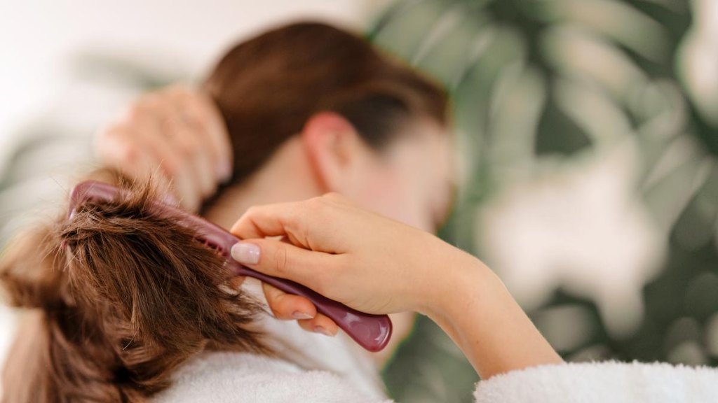 uses for vegetable oil: Rear view of young woman combing her hair. Morning routine concept.