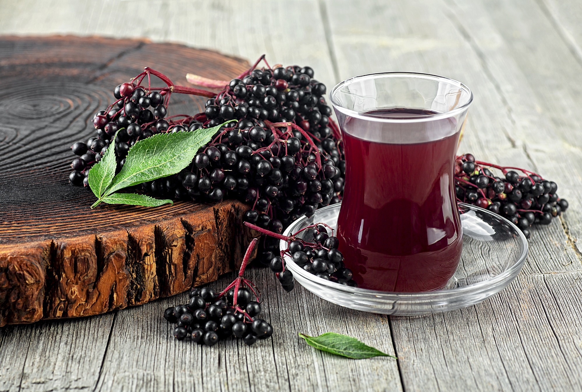 Fresh ripe black elderberries, elderberry syrup and leaves of elderberry on rustic wooden board.