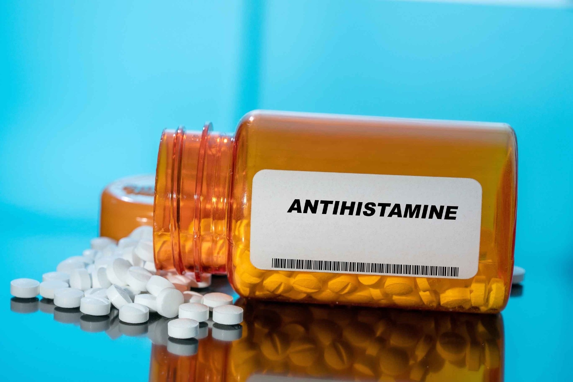 Antihistamine white medical pills and tablets spilling out of a drug bottle.