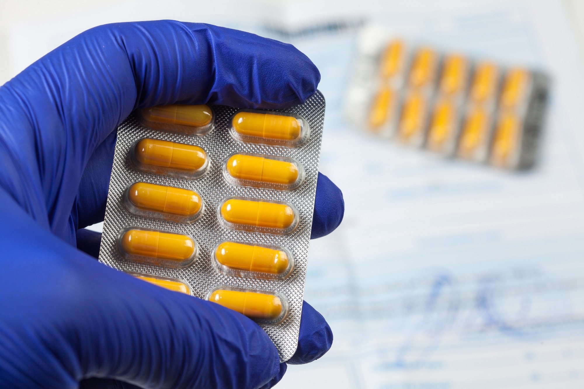 medical practitioner wearing blue surgical latex gloves holding yellow drugs packet.