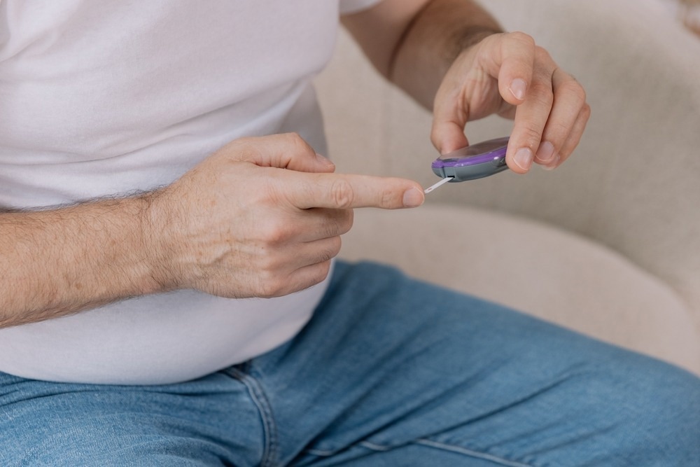 Diabetic senior man on wheelchair checking blood sugar level with fingerstick testing glucose meter.