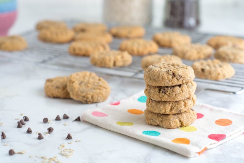 A stack of four Peanut Butter Oatmeal Chocolate Chip cookies sit on a polka-dot napkin next to some mini chocolate chips.