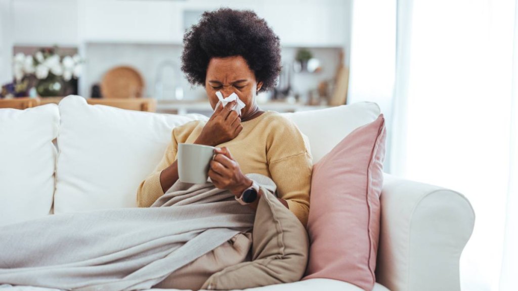 Woman blowing her nose on the couch before taking a cold medicine