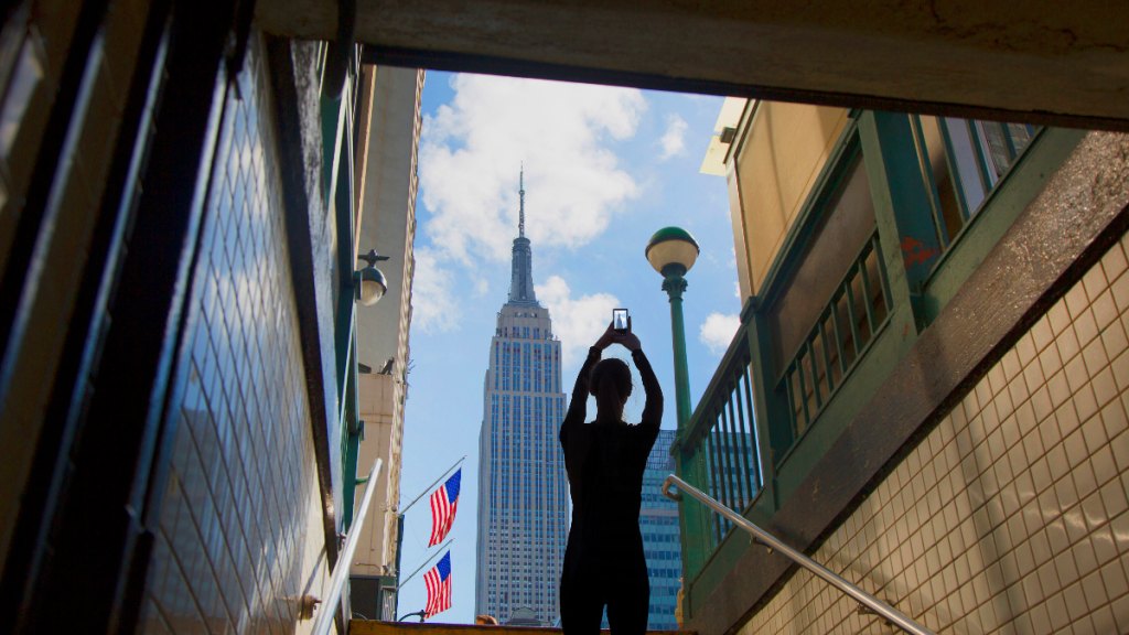 silhouette of a women from behind as she raises her cellphone to snap a picture of the iconic Empire State Building