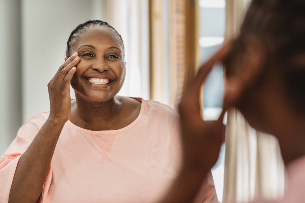 mature woman smiling looking at skin in mirror