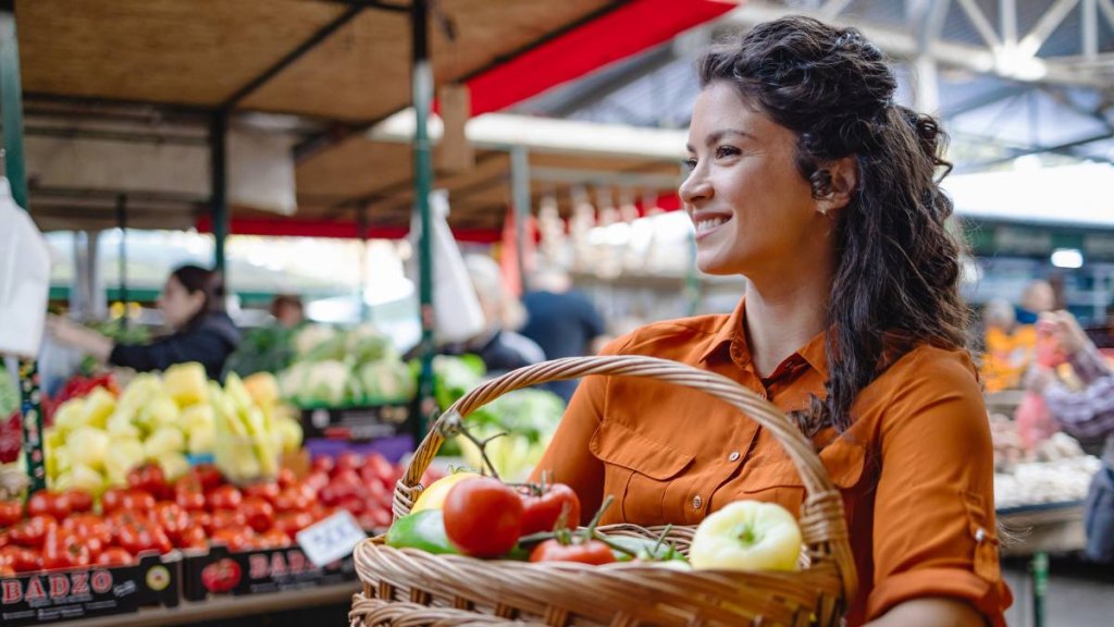 Woman holding fruits and veggies at an outdoor market