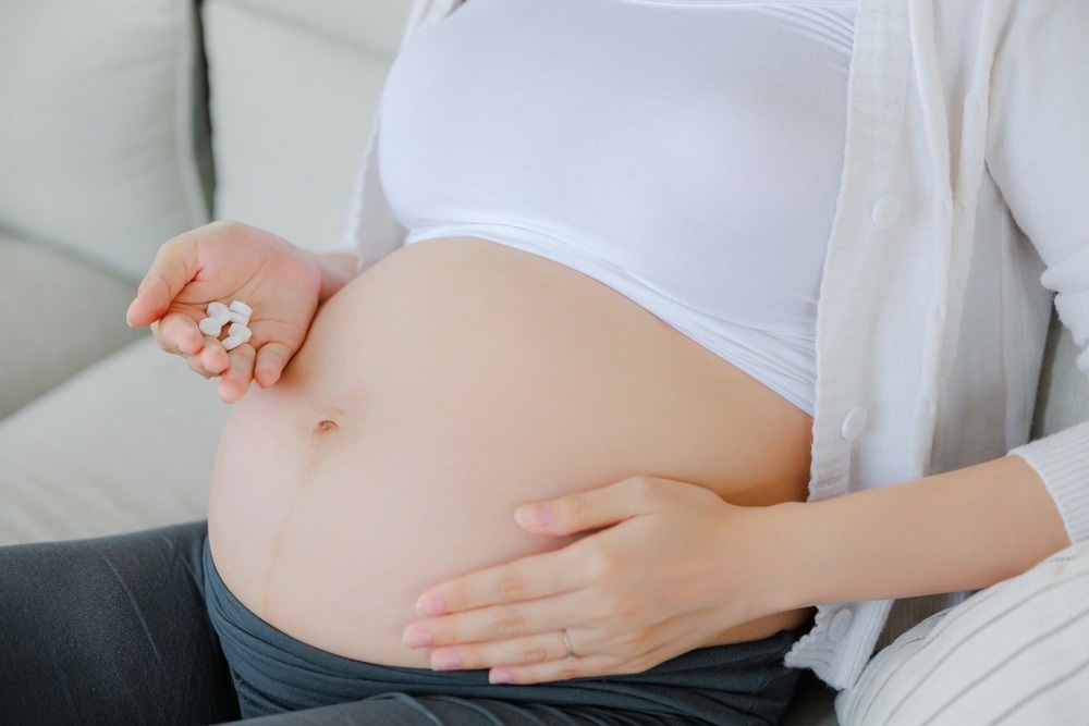 Close up hand of Asian happy pregnant woman with medicine on sofa and touching her belly.