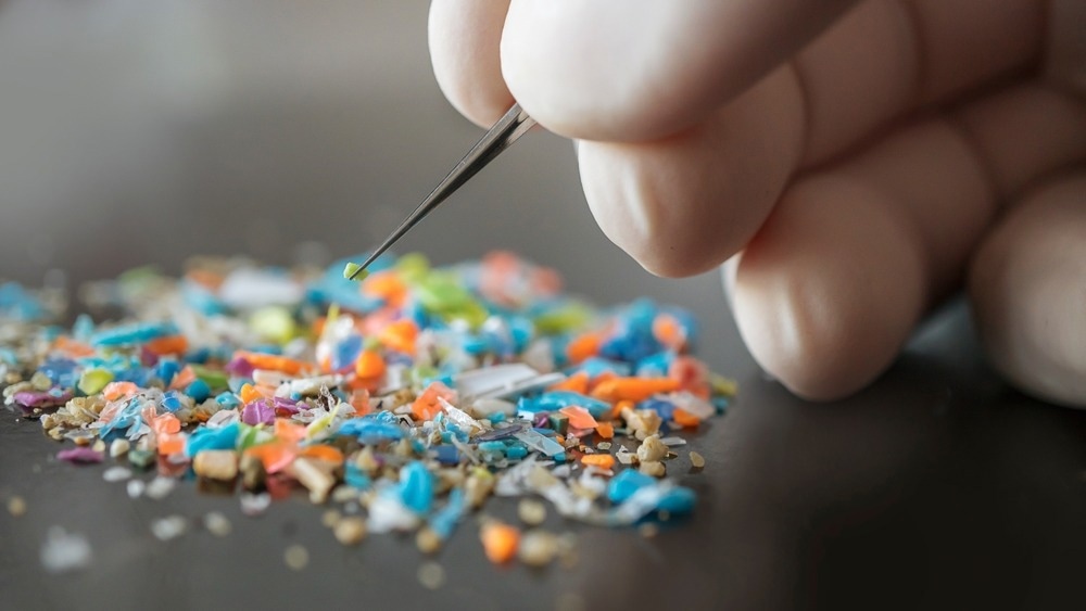 Macro shot of a person with medical gloves and tweezers inspecting a pile of micro plastics.